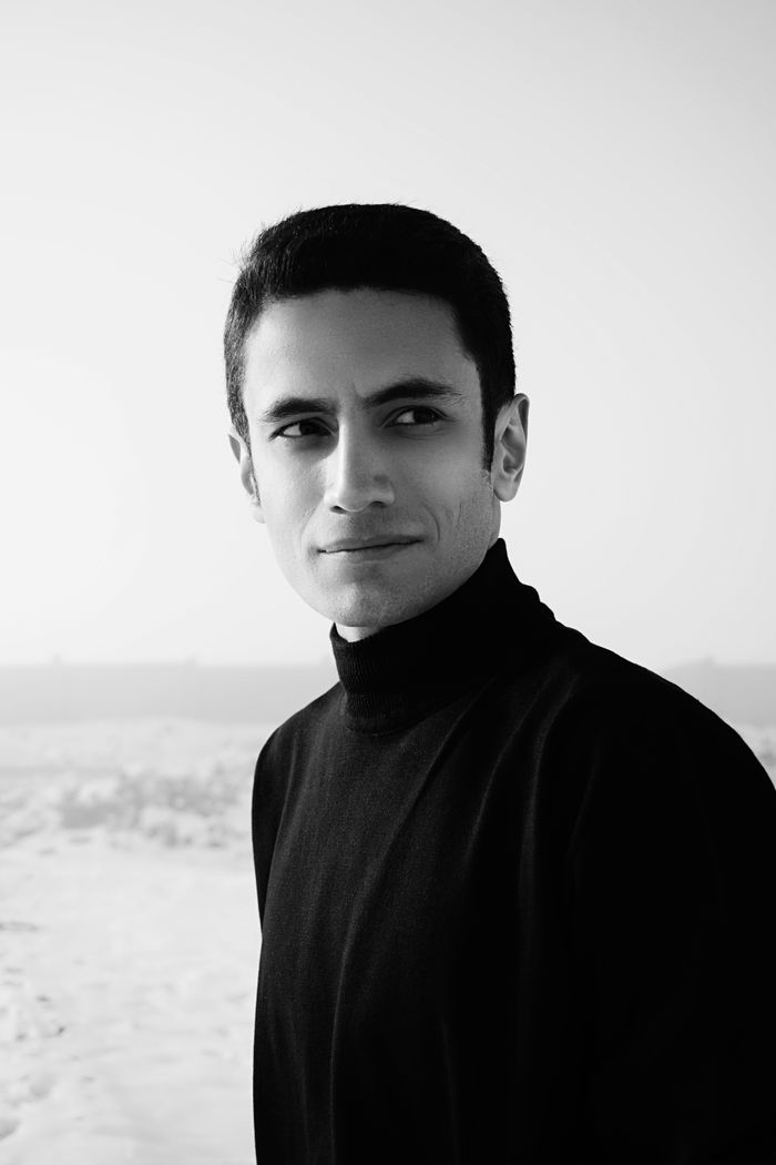 Black and white of young serious male in warm turtleneck standing in middle of snowy area and looking away